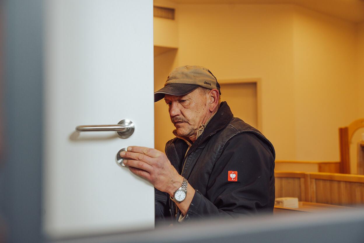 Tür Reparatur Mitarbeiter in dunkler Kleidung in einem hellen Raum bei der Reparatur einer weißen Tür