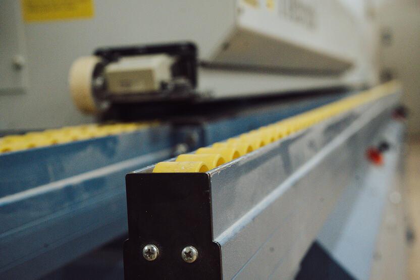 Maschinenhalle Nahaufnahme einer Kantenanleimmaschine mit einer blauen Schiene und gelben Rollen
